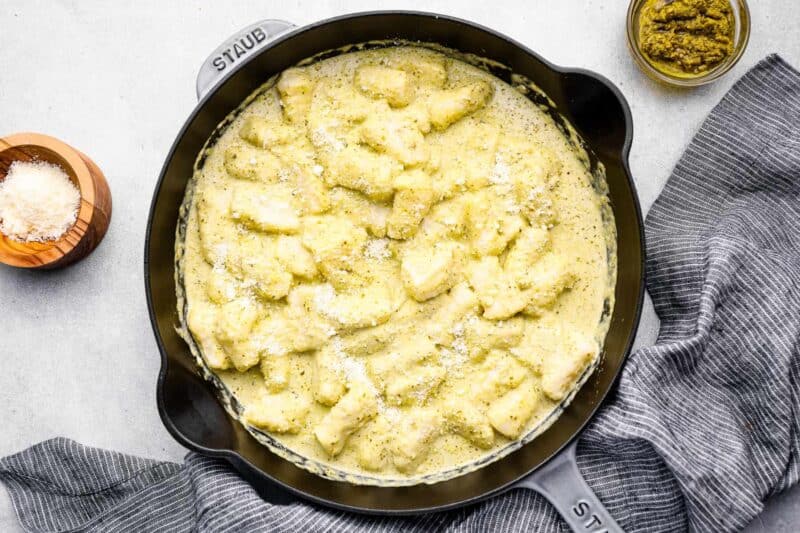 overhead view of gnocchi in pesto cream sauce in a cast iron skillet.