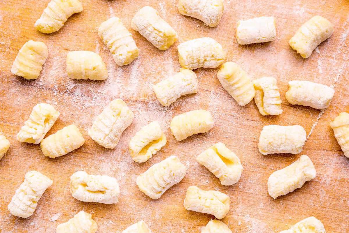 making gnocchi pasta on a wooden cutting board; potato gnocchis are partially coated in flour