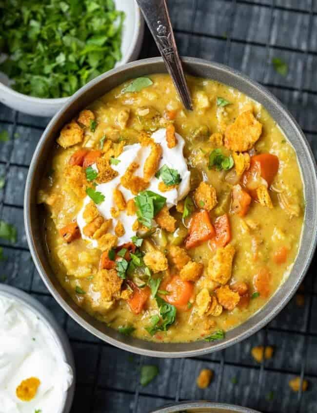 overhead view of a serving of mulligatawny soup in a gray bowl with a spoon.