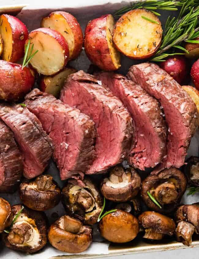 sheet pan with slices of beef tenderloin and roasted red potatoes and mushrooms