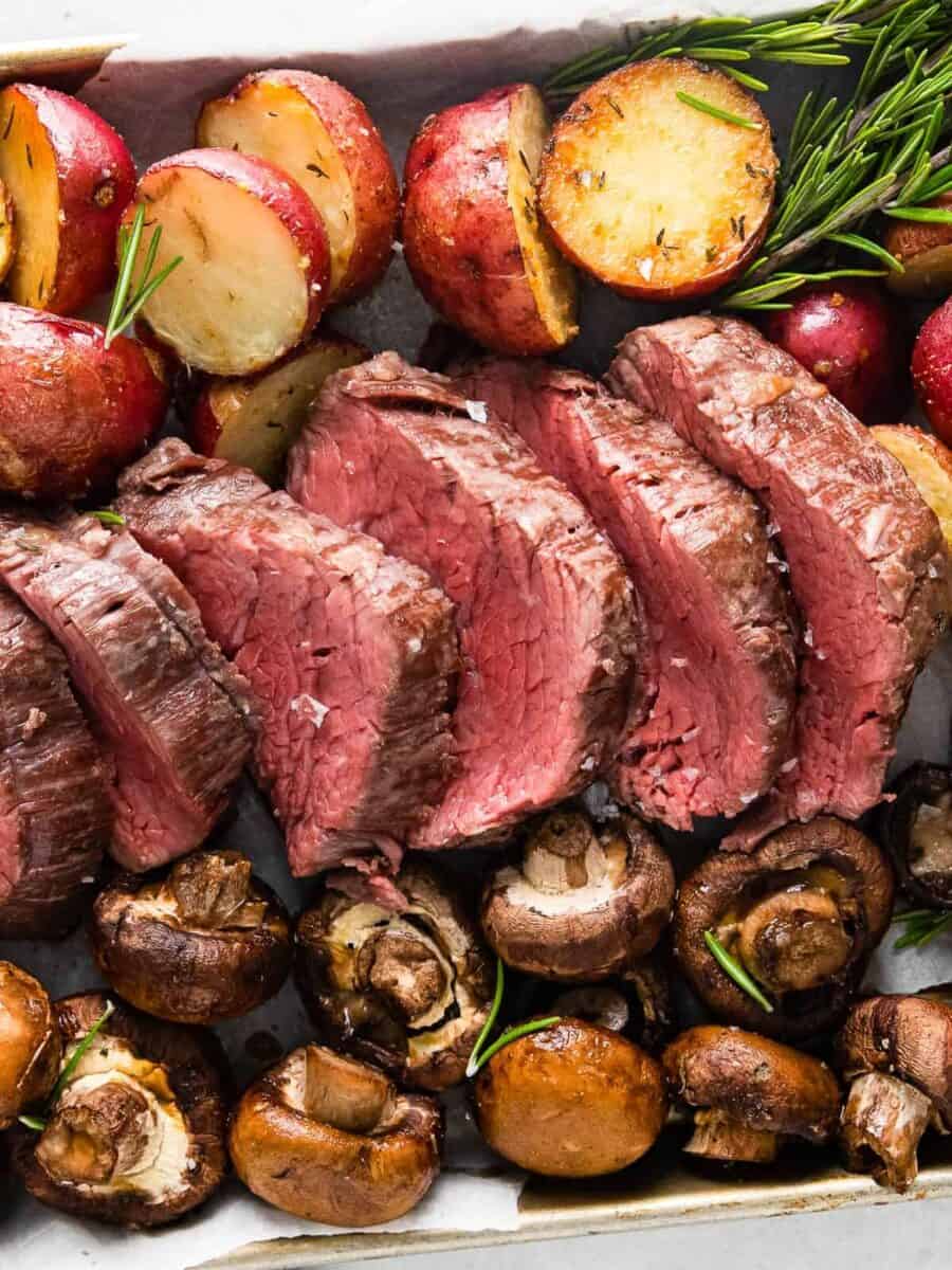 sheet pan with slices of beef tenderloin and roasted red potatoes and mushrooms