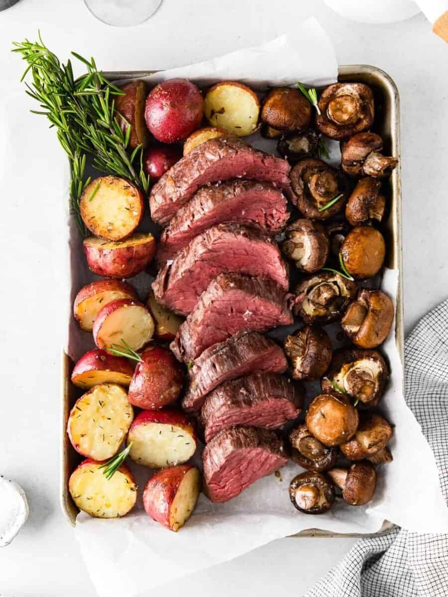 sheet pan with slices of beef tenderloin and roasted red potatoes and mushrooms