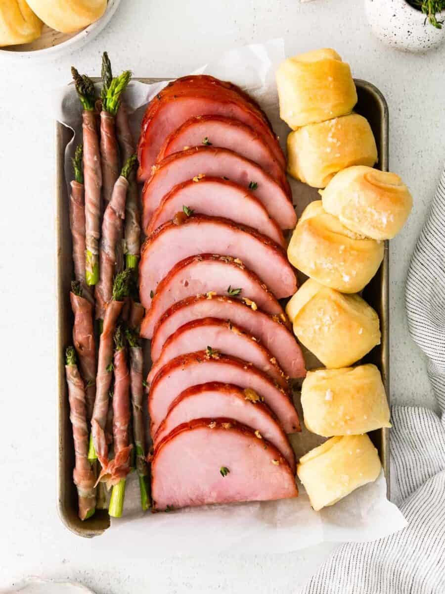 ham, prosciutto wrapped asparagus, and rolls on a sheet pan after baking