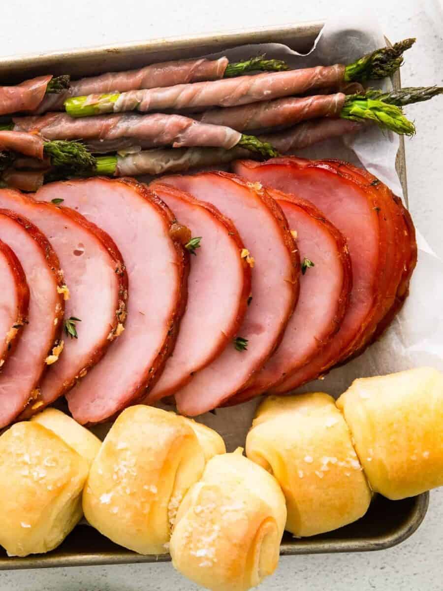 ham, prosciutto wrapped asparagus, and rolls on a sheet pan after baking