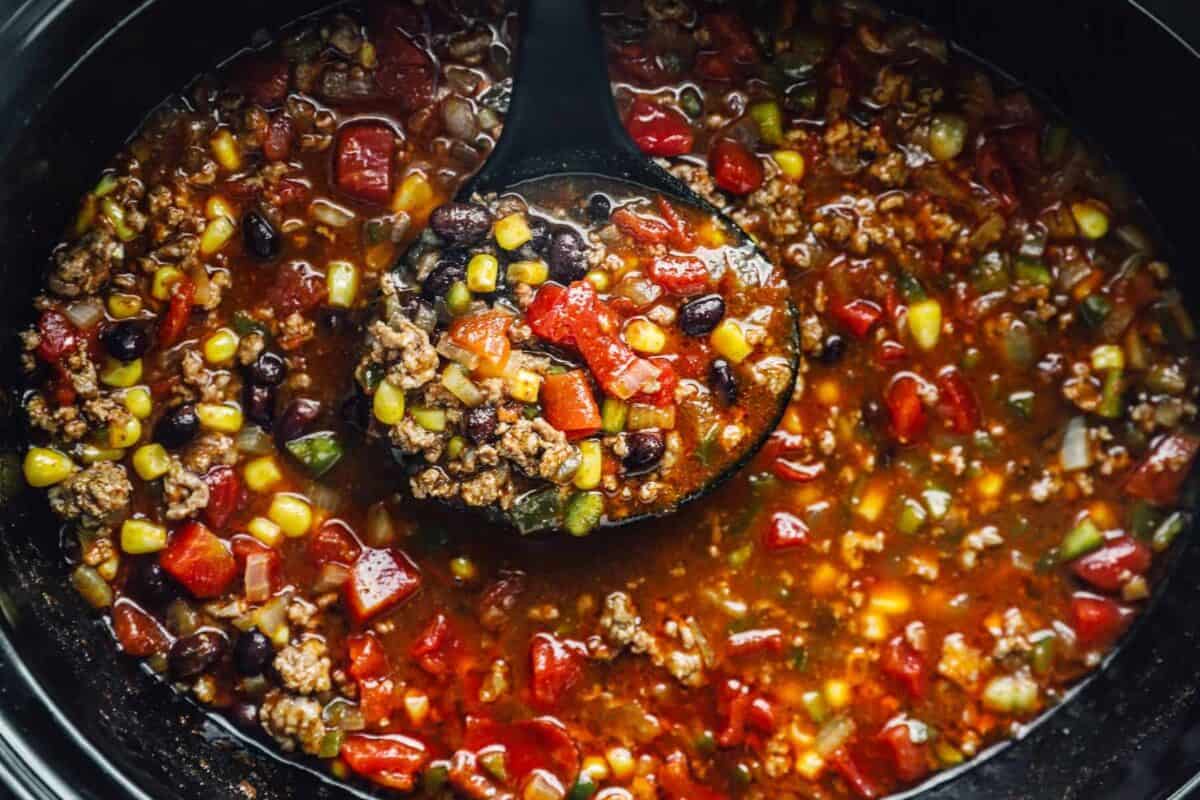 overhead view of a ladle scooping taco soup from a crockpot.