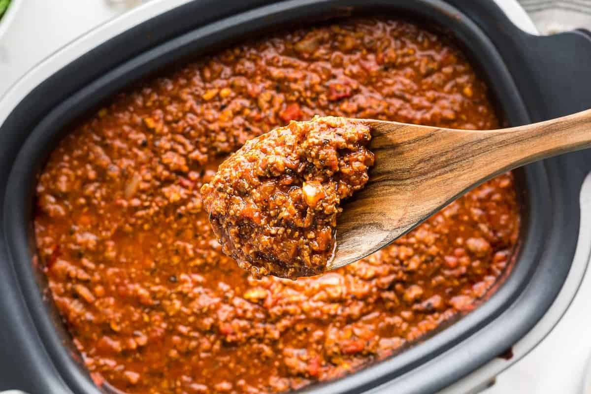 a spoonful of crockpot spaghetti sauce over a crockpot filled with sauce.
