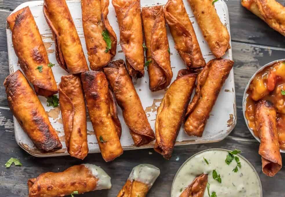 Mini taquitos on wood board, some dipped in sauce