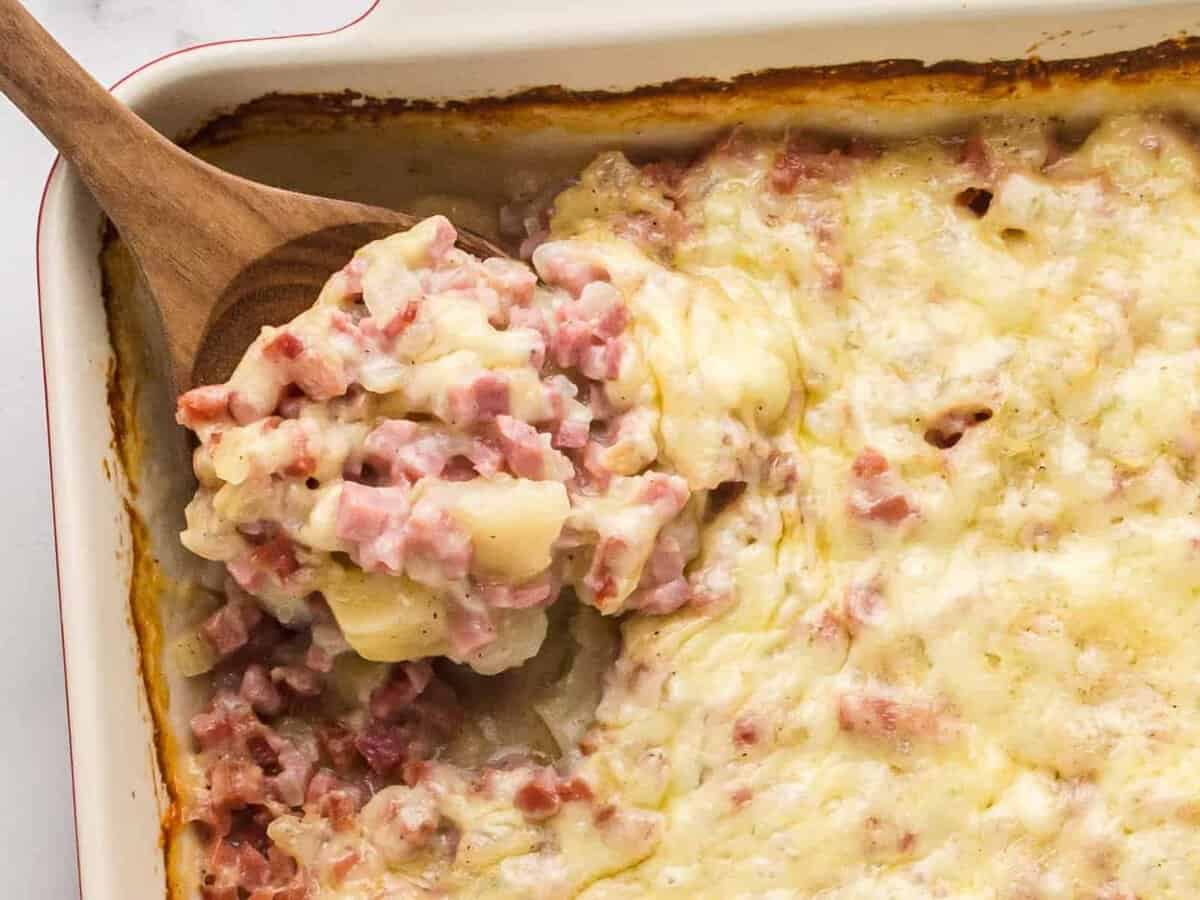 overhead image of ham and potato casserole with a wood spoon with a serving scooped out