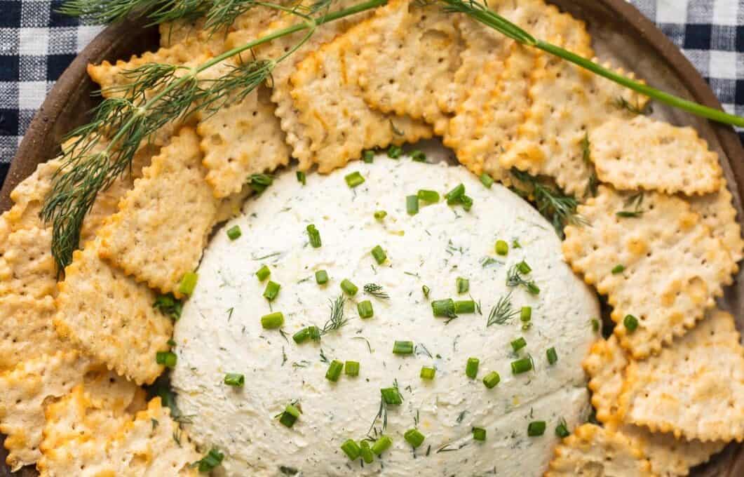 A platter filled with crackers and herb cream cheese dip