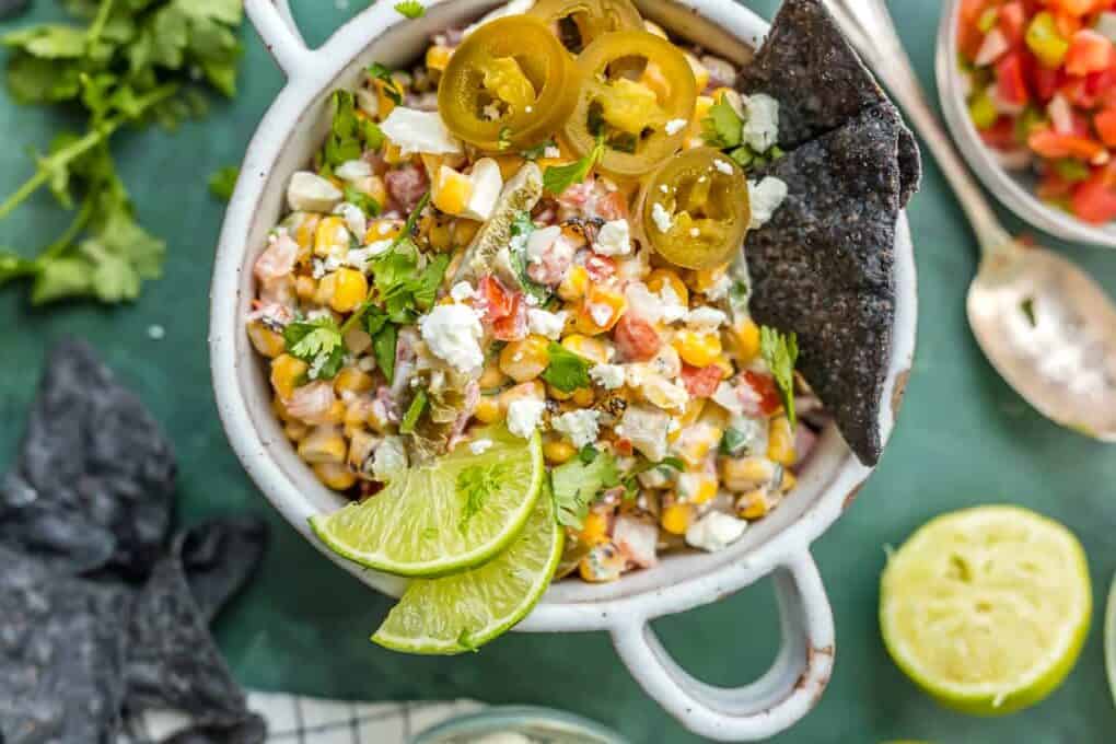 A bowl of Mexican street corn salsa with blue tortilla chips dipped in