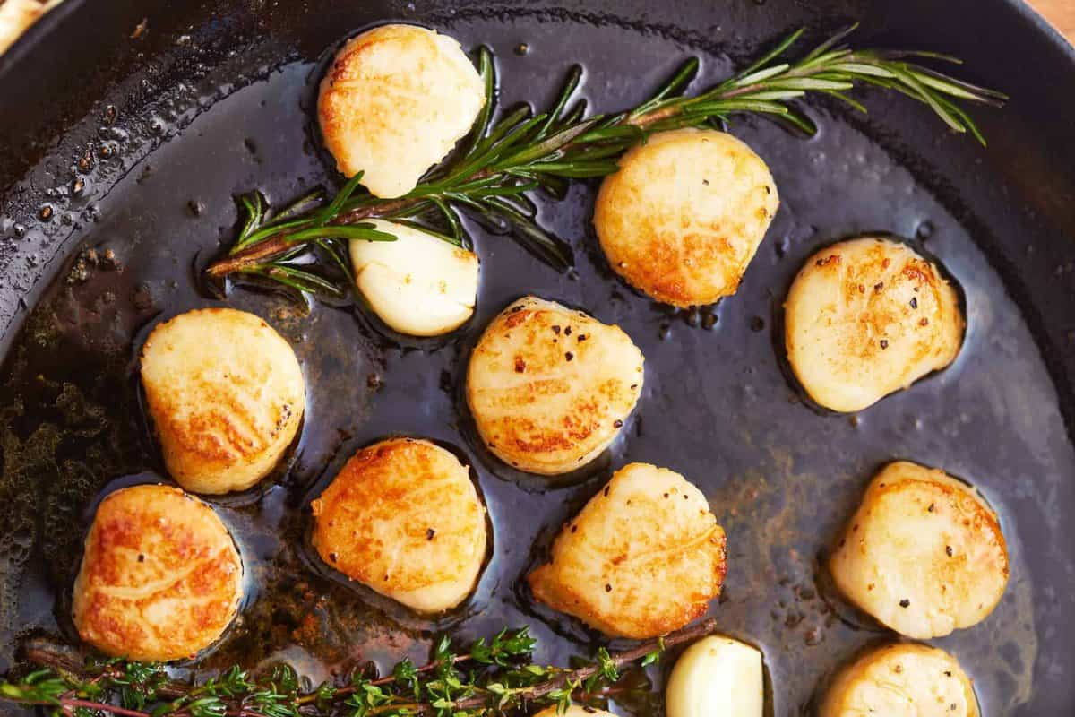 close up view of seared scallops in a cast iron pan with herbs.