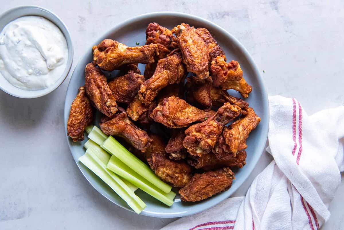 overhead view of trashed wings on a gray plate with celery sticks and ranch.