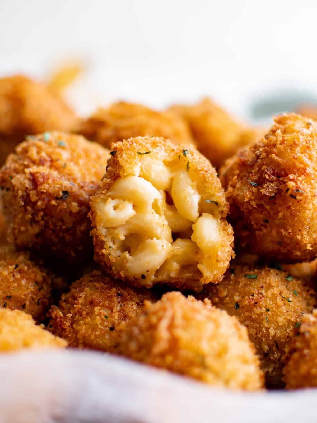 close up on a pile of fried mac and cheese balls; one has a bite taken out of it to reveal the macaroni inside.