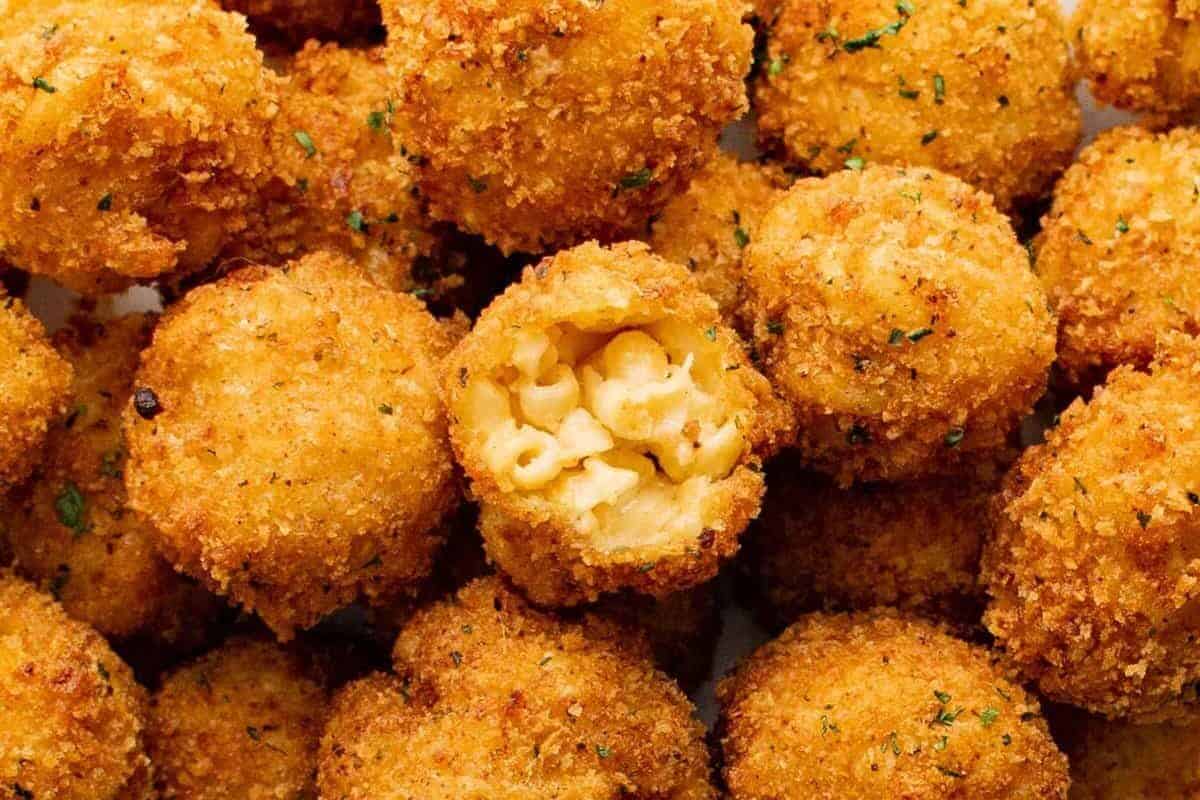 close up on fried Mac and cheese balls, the one at the center has a bite taken out to reveal the Mac and cheese