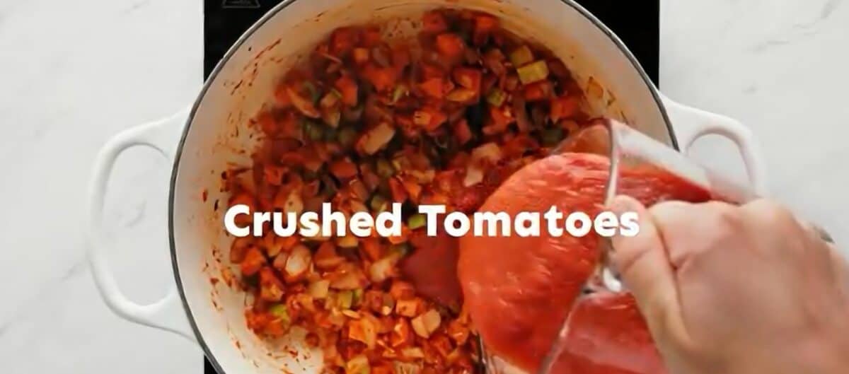Adding crushed tomatoes to the pot of veggies. 
