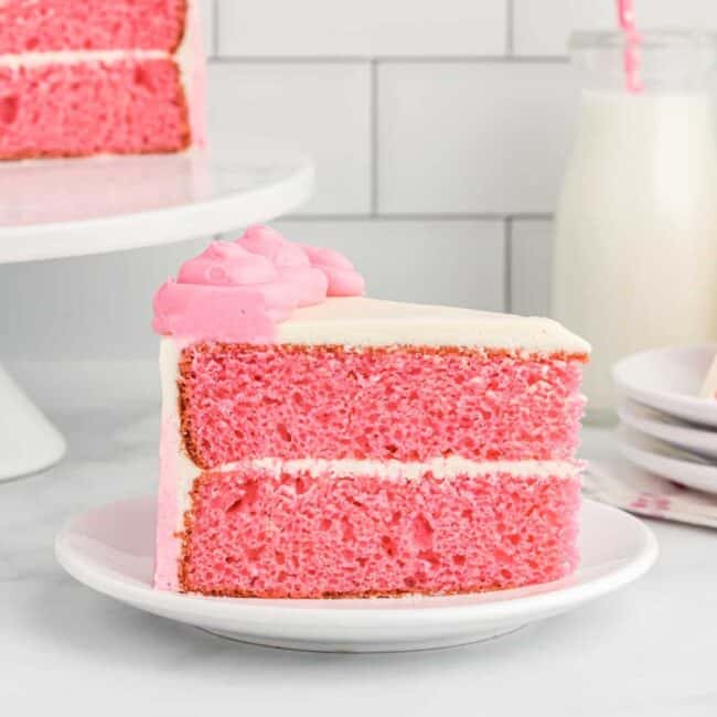 side view of a slice of pink velvet cake on a white plate.