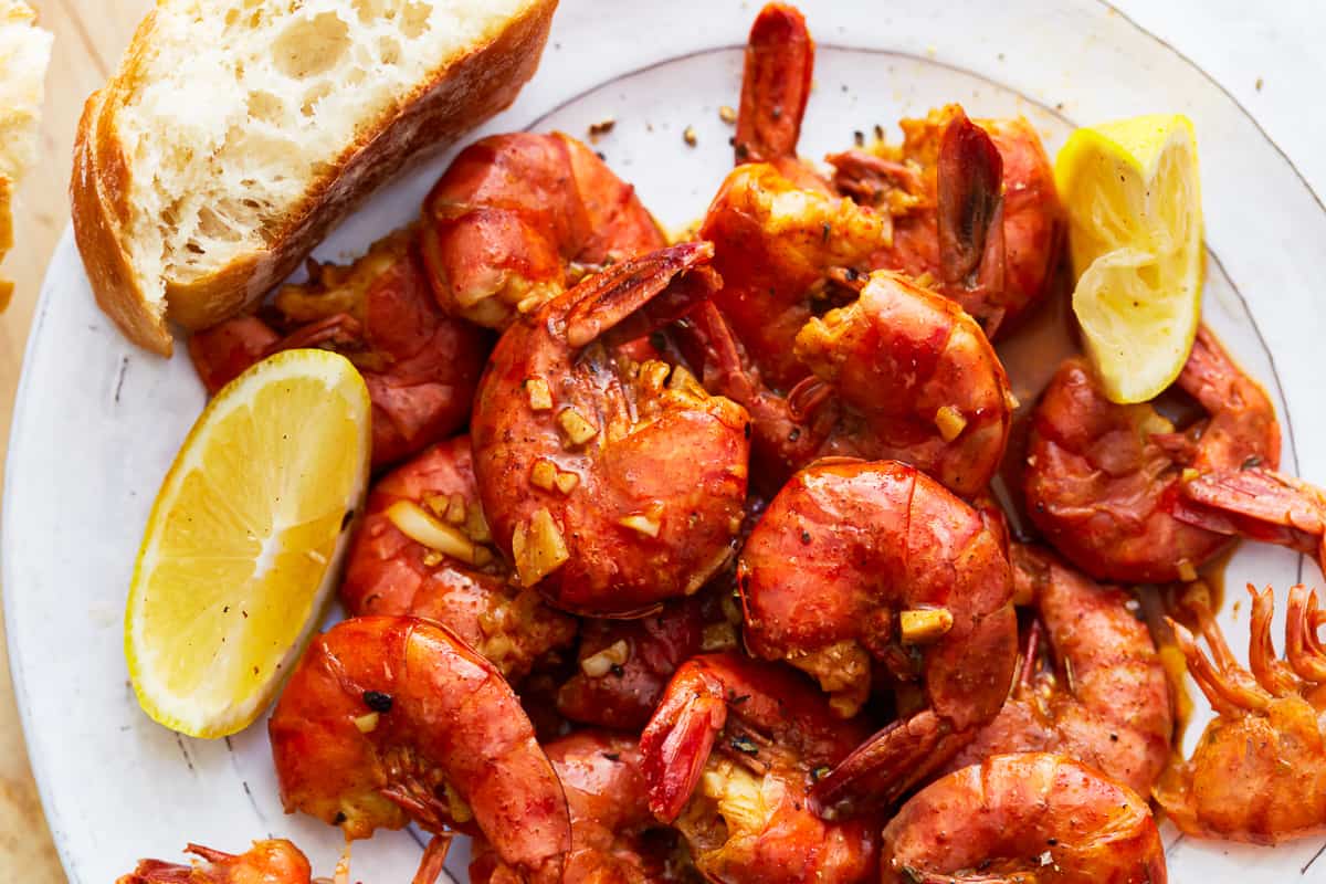 BBQ shrimp on a plate with bread and lemon wedges.