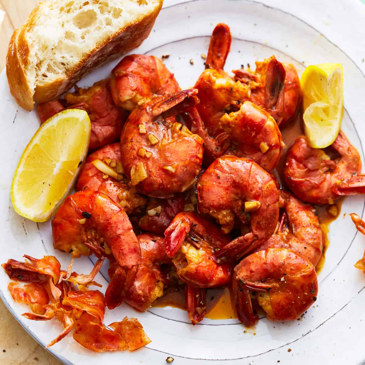 A plate with BBQ shrimp and bread on it.