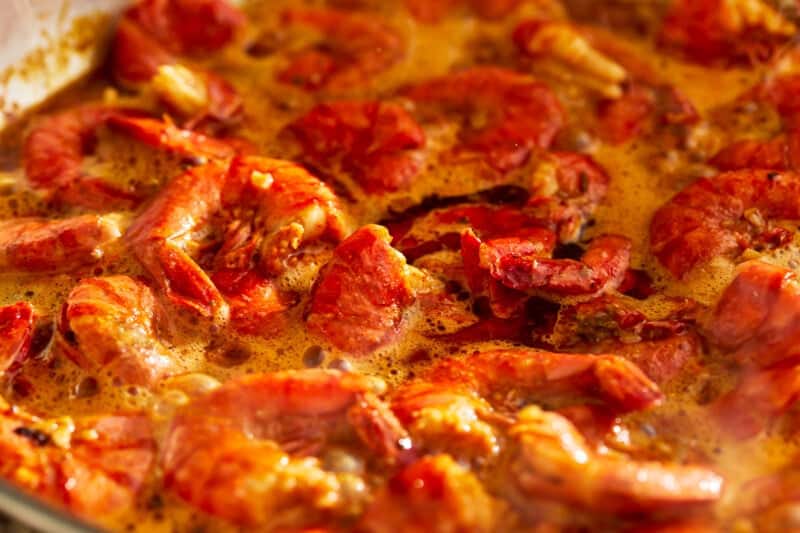 A sizzling pot of bbq shrimp in a savory sauce on a stove.