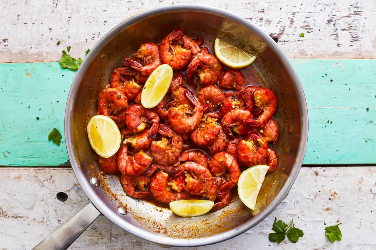 New Orleans bbq shrimp in a frying pan with lemon wedges.