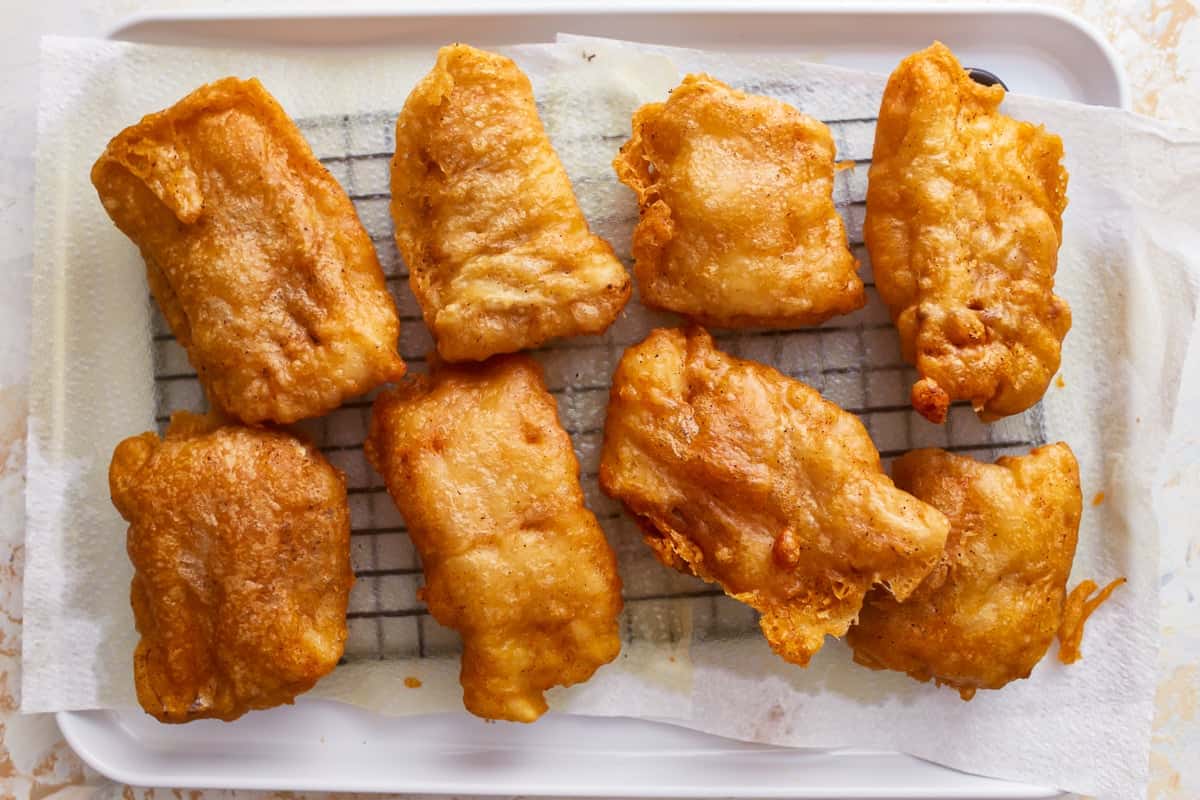 Deep-fried pieces of beer battered fish on a cooling rack.