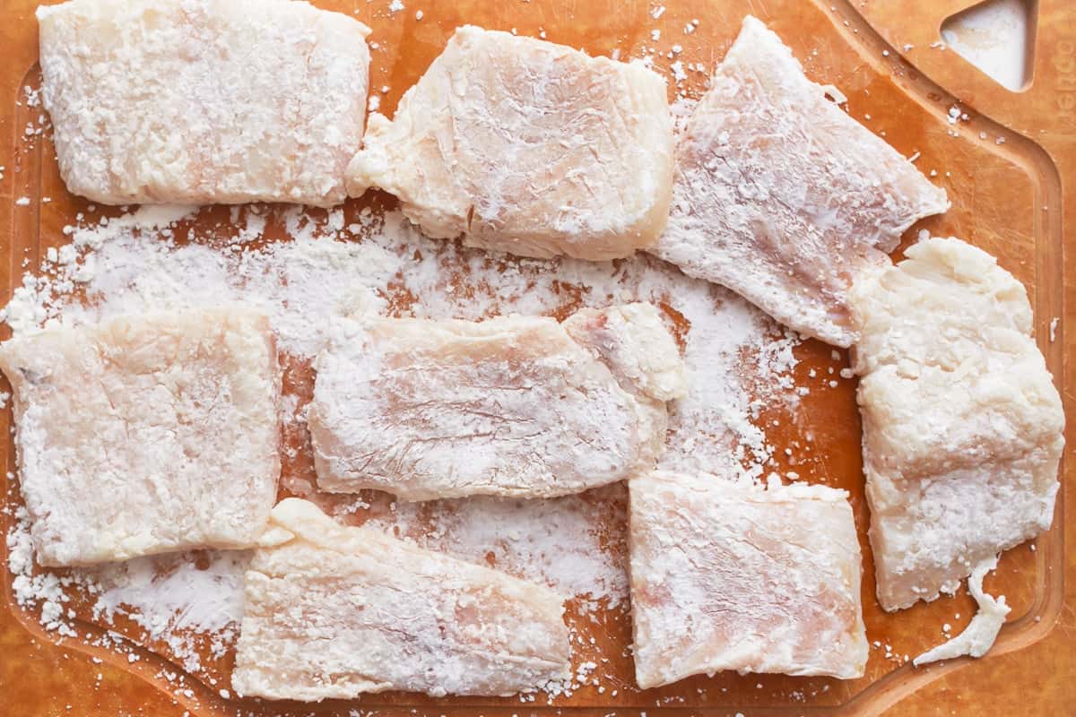 Raw fish fillets dipped in cornstarch on a cutting board.
