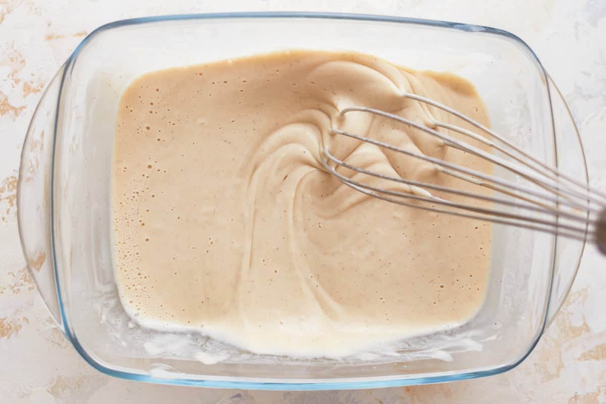 beer batter in a glass dish with a whisk.