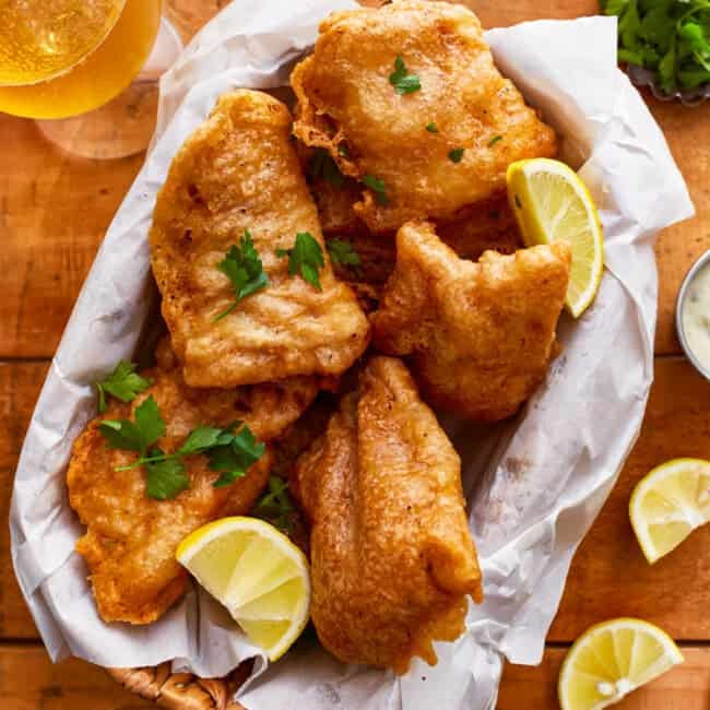 Beer battered fish and chips with lemon wedges on a wooden table.