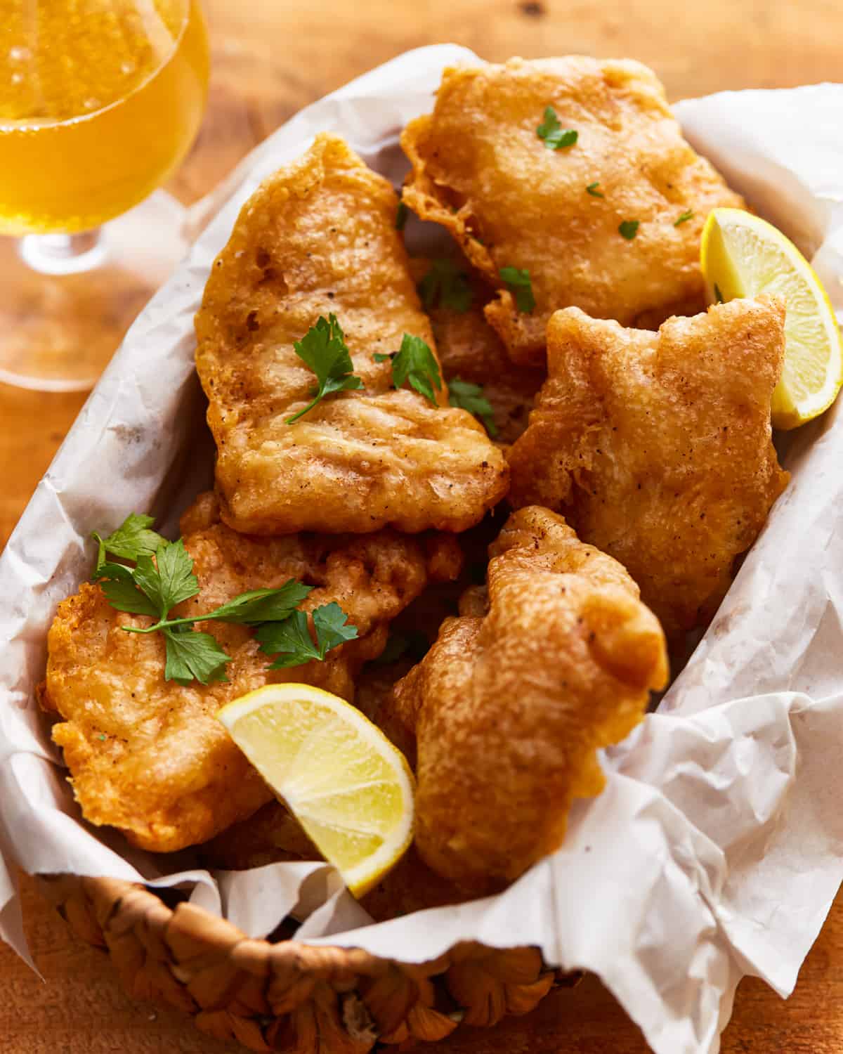 Beer battered fish in a basket with lemon wedges.