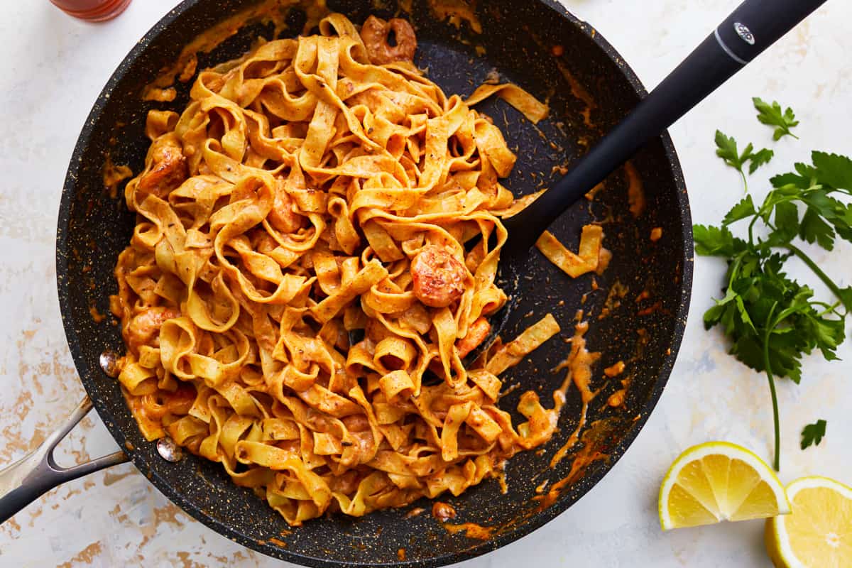 Blackened shrimp fettuccine alfredo pasta in a skillet with lemon and parsley.