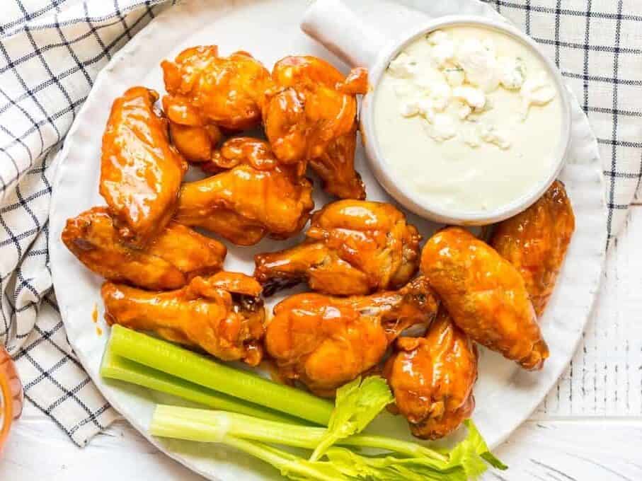 A plate of baked buffalo wings with blue cheese ranch and celery