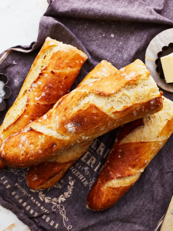 A bunch of french baguette on a table with butter and a knife.