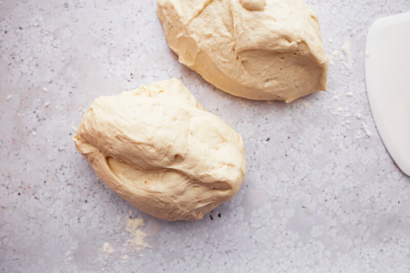 Two pieces of dough, resembling french baguettes, on a table next to a knife.
