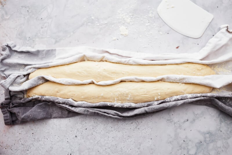 A French baguette on a white cloth on a marble table.