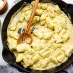 overhead view of gnocchi in pesto cream sauce in a cast iron skillet with a wooden spoon.