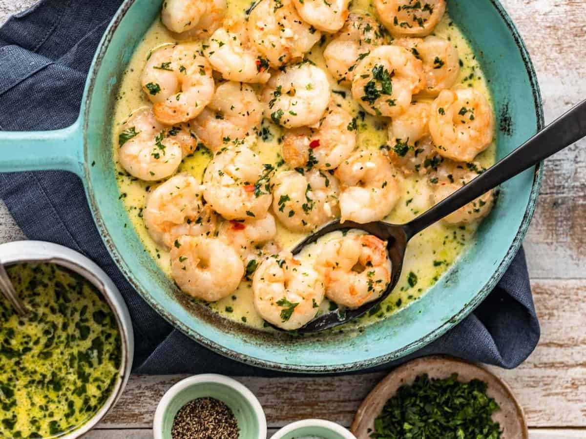 creamy garlic shrimp in a blue pan with a spoon.