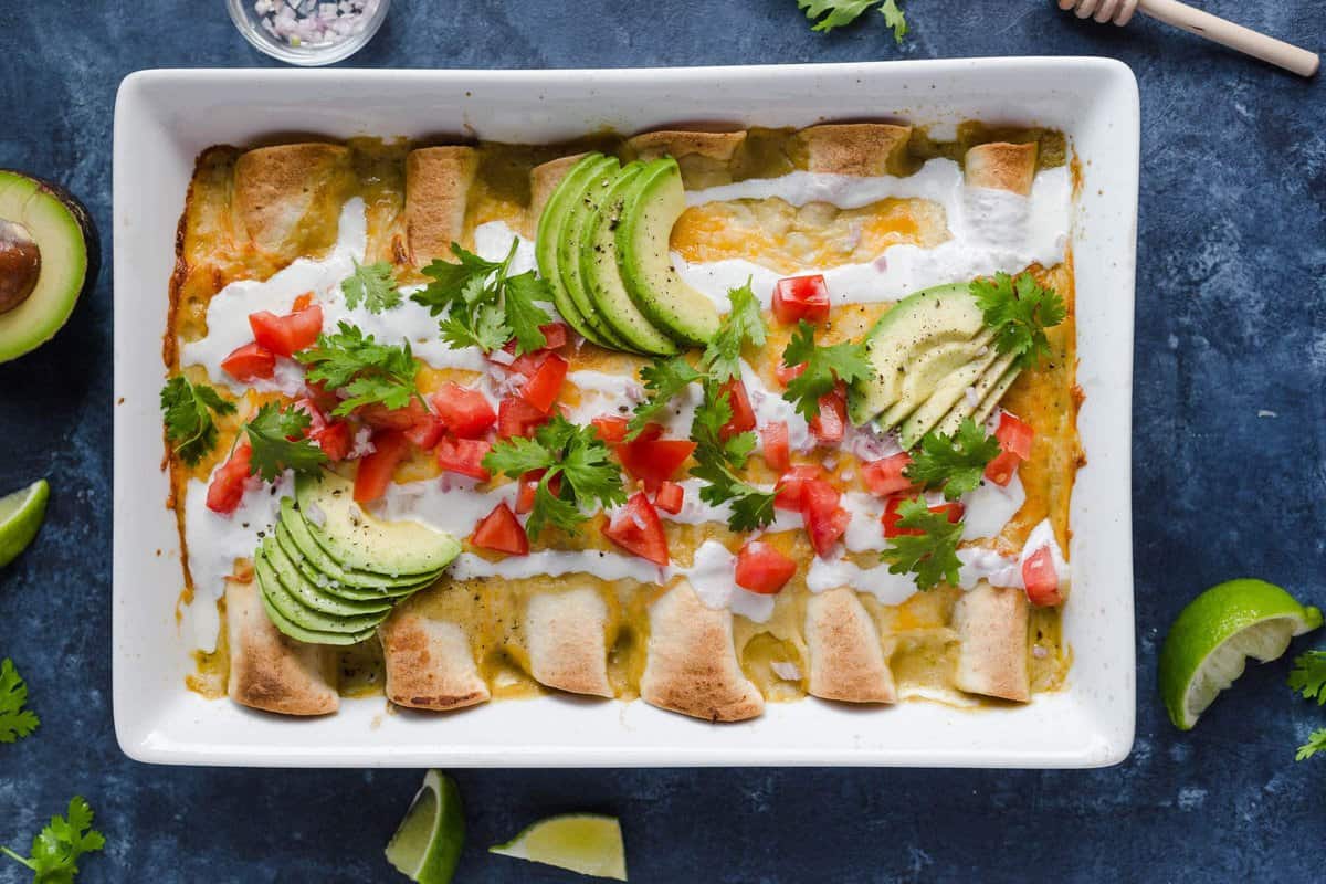 A baking dish full of easy chicken enchiladas made with cheese, sour cream, enchilada sauce, and more