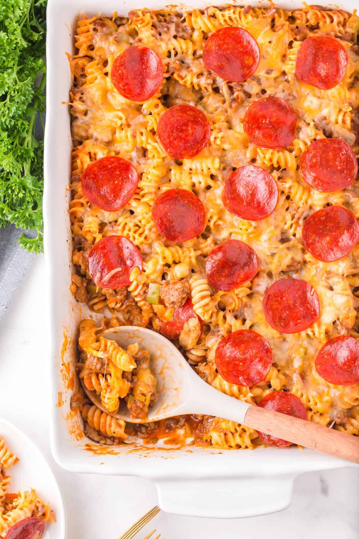 A casserole dish with pepperoni pizza and a spoon.