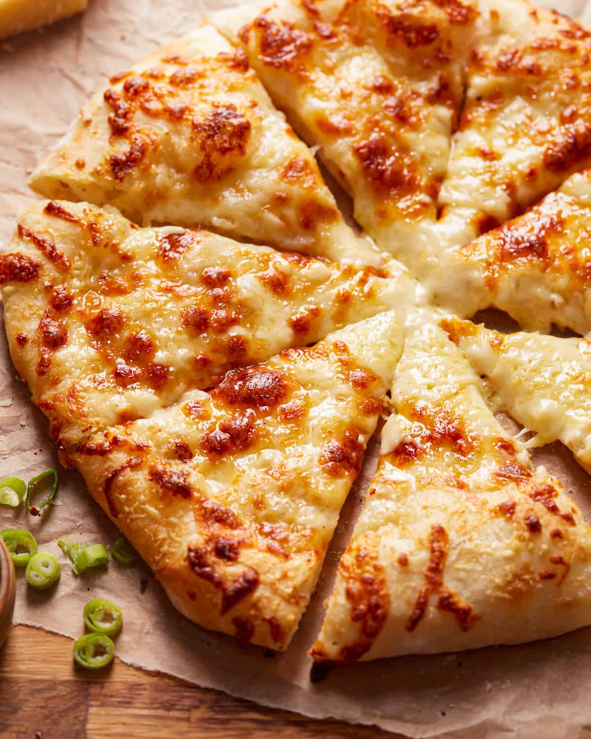 A pizza with cheese and green onions on a wooden board.
