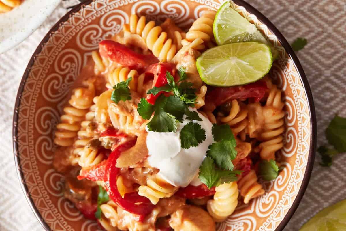 overhead view of chicken fajita pasta in a patterned bowl with lime wedges.