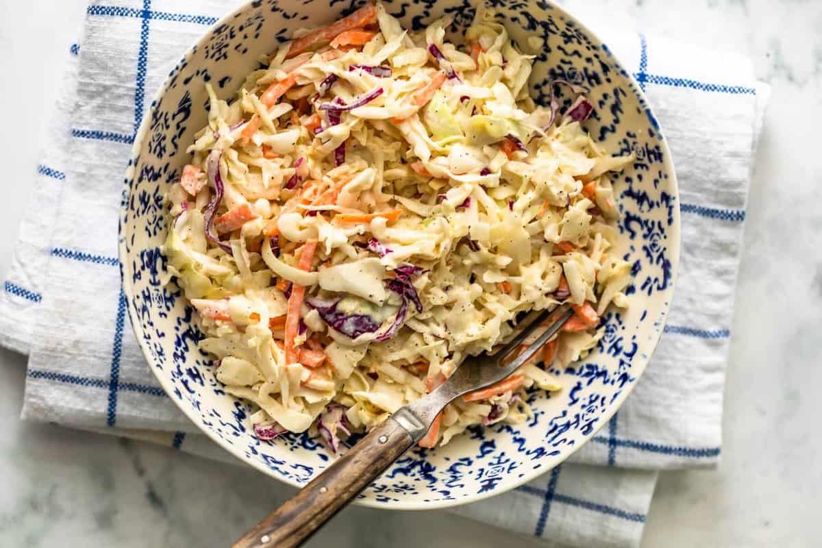 Overhead view of coleslaw in a blue and white bowl with a fork on a dish towel.