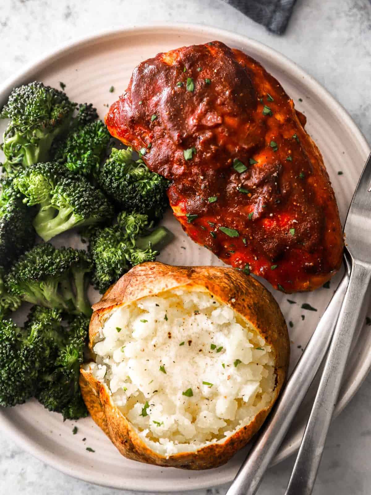 slow cooker barbecue chicken on a plate with broccoli and a baked potato