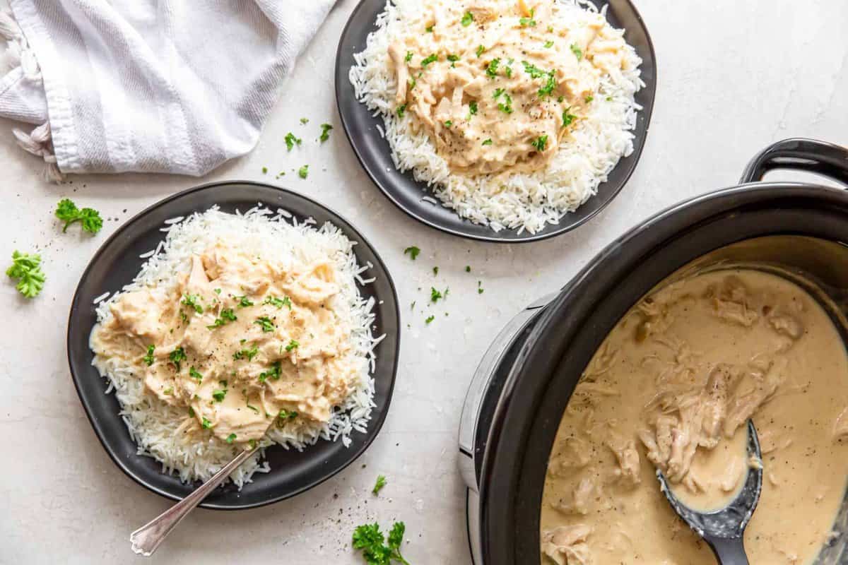 servings of crockpot chicken and gravy over rice on black plates.
