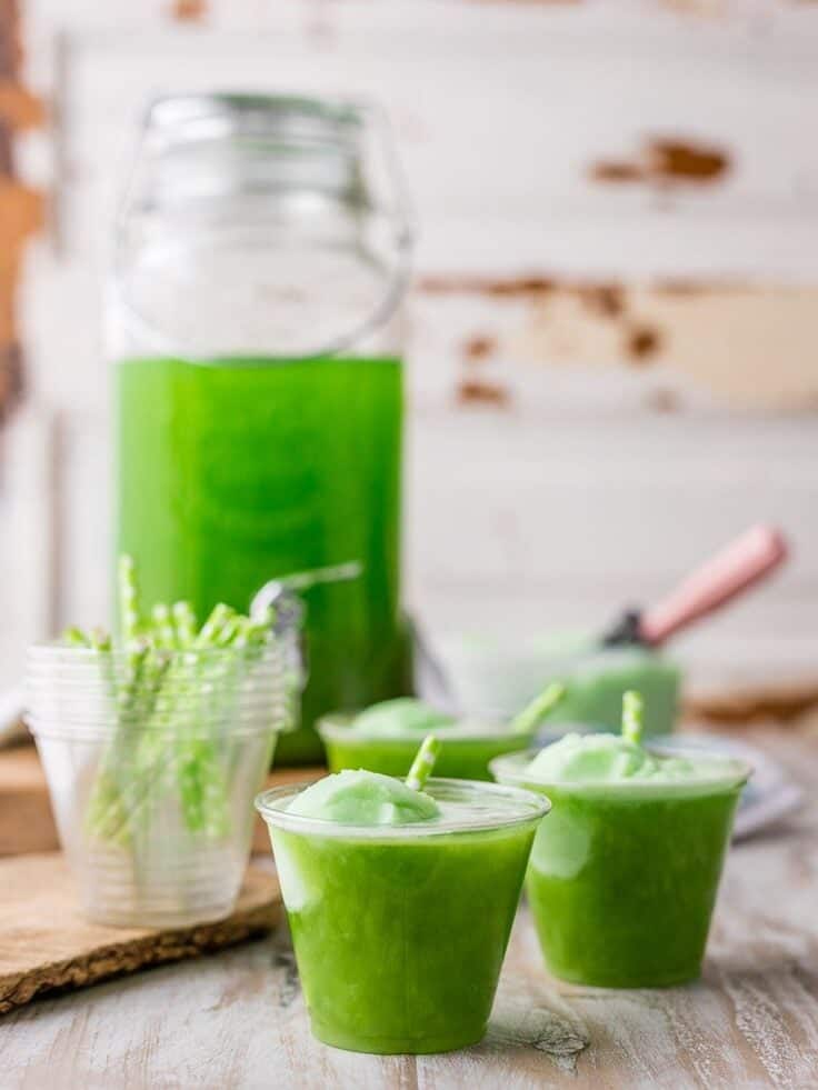 cups of green party punch in the foreground, with cups full of straws next to it