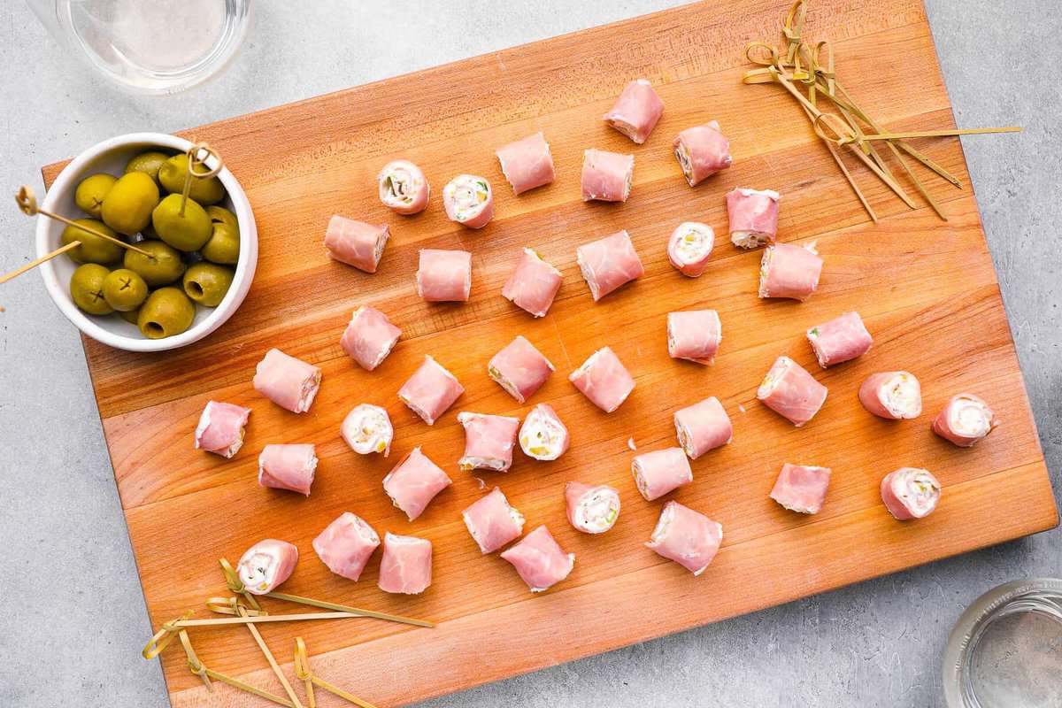 ham roll ups on a wooden cutting board with a side of pickles.