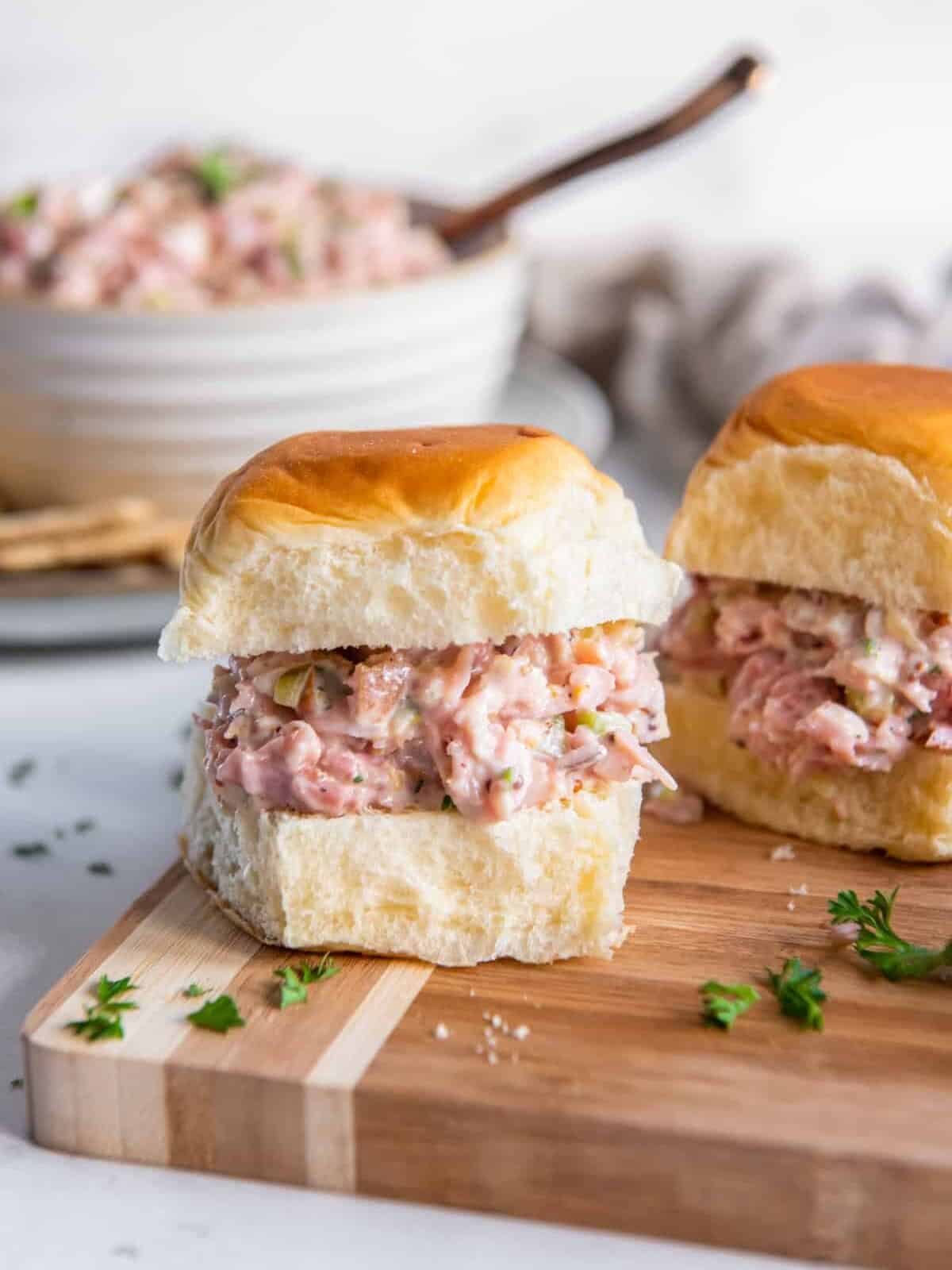 ham salad on slider rolls on a wooden cutting board.