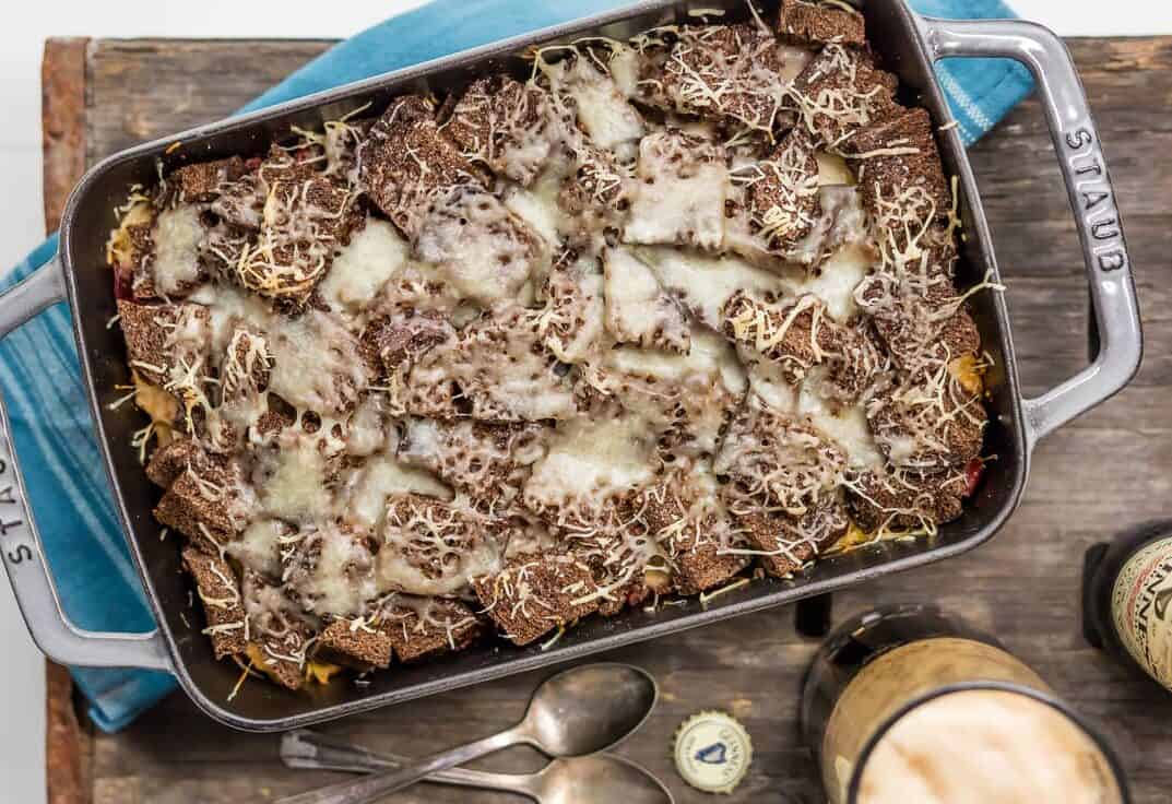 overhead view of corned beef casserole topped with rye bread and Swiss cheese, on a rustic table top background