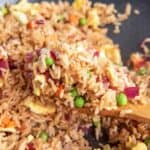 close up view of a wooden spoon lifting a scoop of vegetable fried rice from a wok.