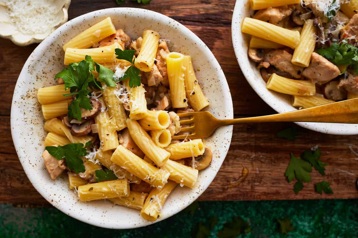 overhead view of a serving of chicken mushroom pasta in a white bowl with a fork.