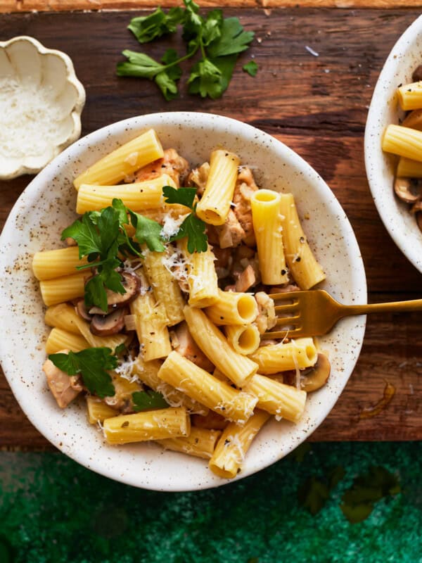 overhead view of a serving of chicken mushroom pasta in a white bowl with a fork.